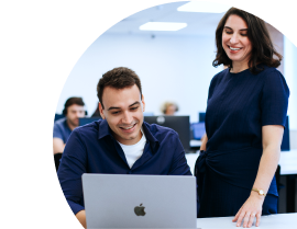 Moça em pé e rapaz sentado olhando para um notebook