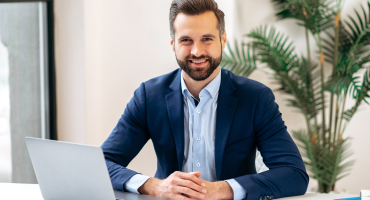 Homem sorrindo, sentado na mesa de seu escritório