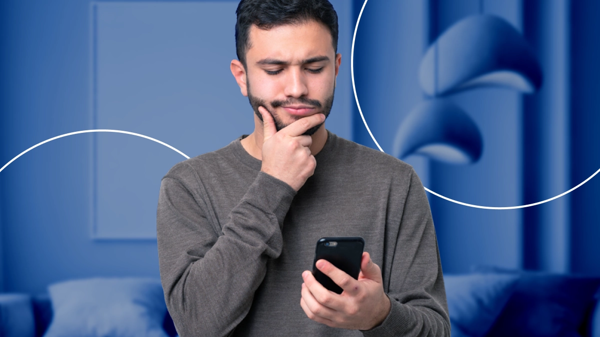 Homem pensativo, com a mão no queixo, segurando e olhando para o celular